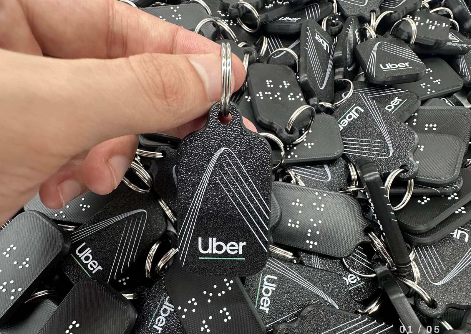 A hand holds a black Uber keychain with braille text, above many more